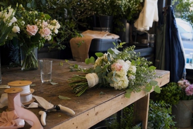 A florist’s wooden workbench with a half-made bouquet of pale roses, ribbon spools and shears, part of the events industry