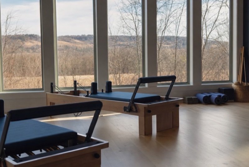 Pilates studio with several reformers facing tall windows, early light falling across pale floorboards
